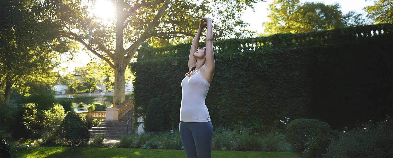 Une femme en tenue de sport se tient dans le parc et s'&eacute;tire.
